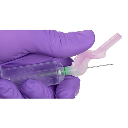 A hand wearing a purple nitrile glove holds a clear plastic syringe with a pink needle protector and a thin metal needle against a plain white background.