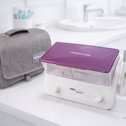 Dental care products including a purple container, white device, and gray bag on a white surface.