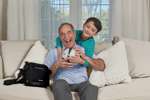 Senior man using iGo2 Portable Oxygen Concentrator, smiling with young boy at home.