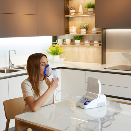 Woman using an inhaler in a modern kitchen with a white cabinet and marble countertop.